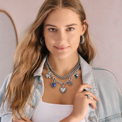 Model wearing layered Brighton silver-plated charm necklaces with heart pendants and coordinating Brighton hoop earrings
