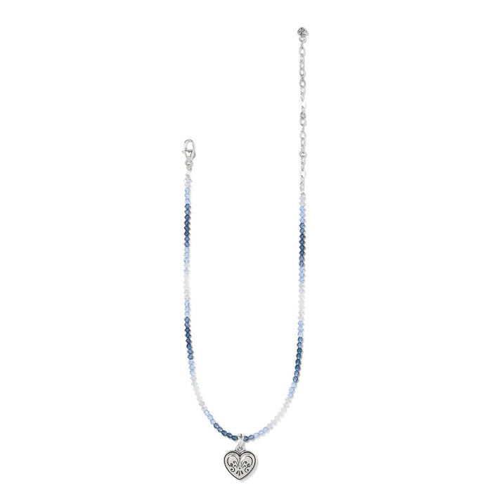 Brighton beaded necklace with blue beads, silver-plated chain, and engraved heart pendant on a white background