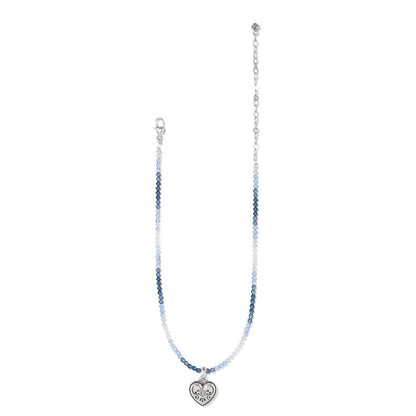 Brighton beaded necklace with blue beads, silver-plated chain, and engraved heart pendant on a white background