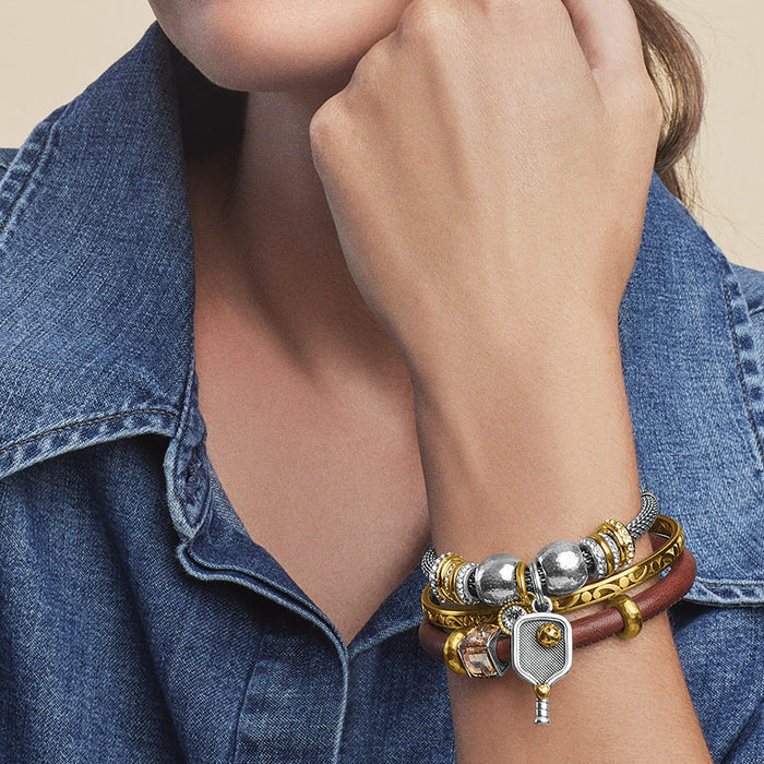 Model wearing stacked Brighton two-tone bracelets with silver beads, brown leather band, and pickleball paddle charm