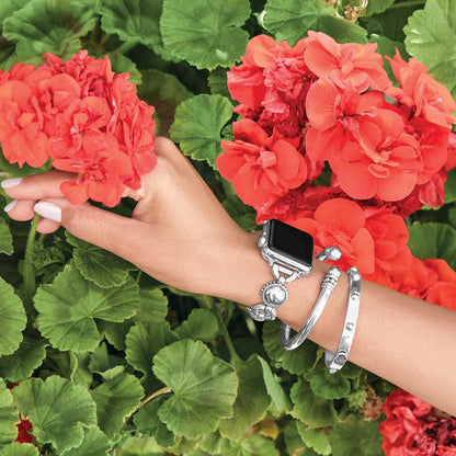 A woman's hand wearing an Apple Watch with Pretty Tough Bold Watch Band and silver bracelets holds a vibrant red geranium flower within a lush green garden backdrop.