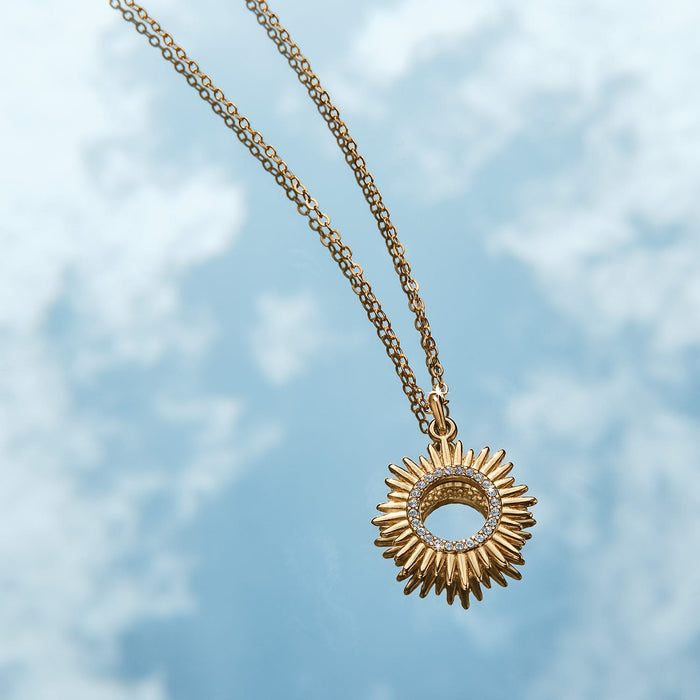 Brighton gold-plated sunburst pendant necklace with crystal accents and delicate chain on a cloudy sky background