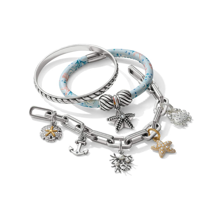Brighton bracelets styled with silver bangle, blue printed band, and two-tone charm chain featuring starfish and anchor charms